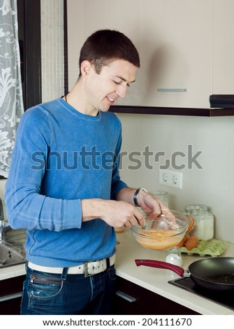 Man making scrambled eggs in frying pan at home kitchen