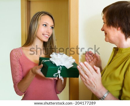 Smiling young girl presenting a gift to elderly female indoor