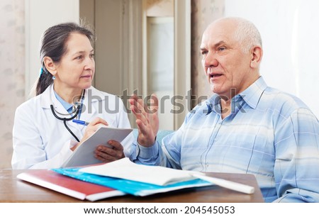 mature doctor talks with sick senior man at near table with documents