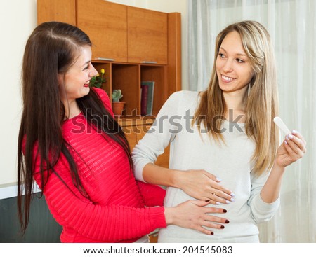 Smiling girls with pregnancy test at home interior. Focus on blonde girl