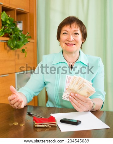 Happy smiling elderly woman sitting with money and documents at the table