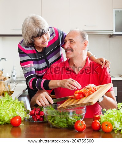 elderly couple cooking with tomatoes in kitchen at home