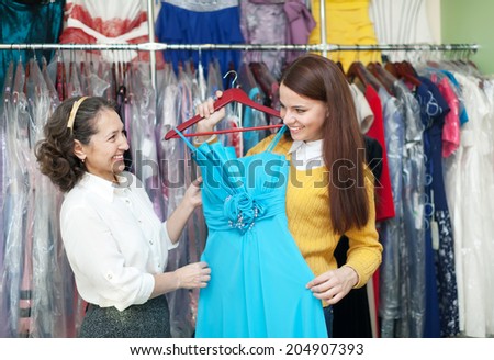 girl chooses evening dress at clothing boutique. Cconsultant helps her