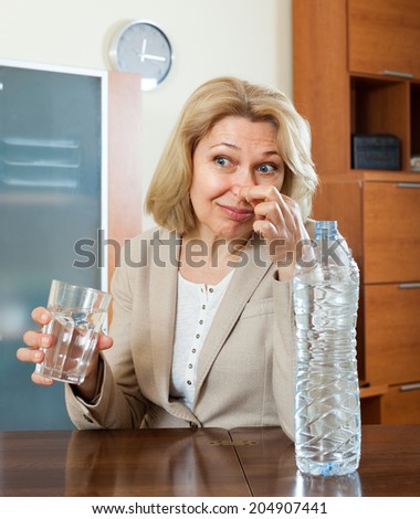 Sad mature woman with grass of poor quality water  at home