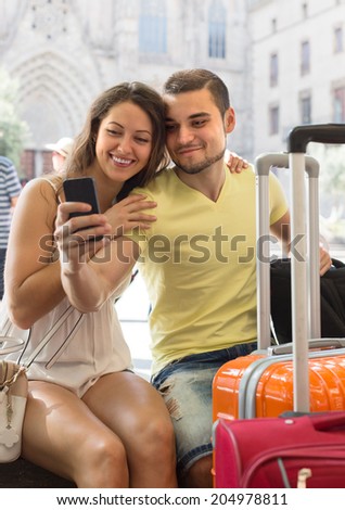 Young couple with luggage doing selfie at travel destination background