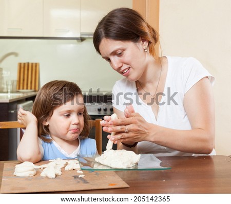 Mom teaches the girl to mold dough figurines in the room