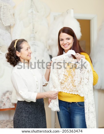 bridesmaid with bride chooses bridal clothes at shop of wedding fashion