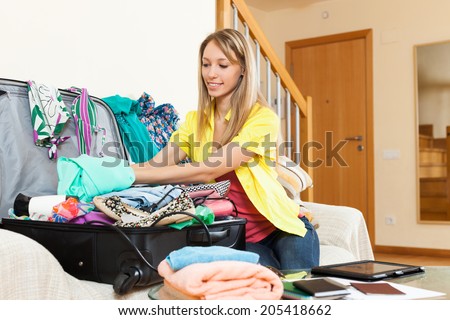 Smiling attractive girl sitting on sofa and packing luggage