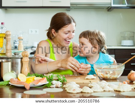 Positive woman with a smiling girl dumplings fish cooking together at home kitchen