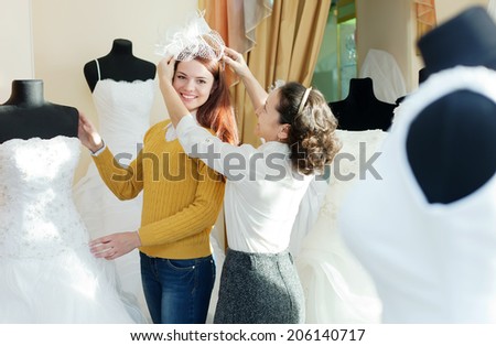 Female shop consultant helps girl chooses white bridal outfit at shop of wedding fashion