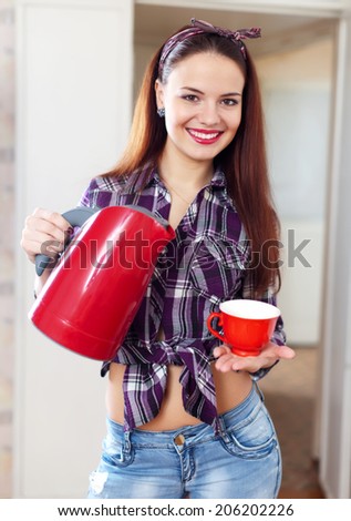 Portrait of happy pretty housewife with red tea kettle and cup at home