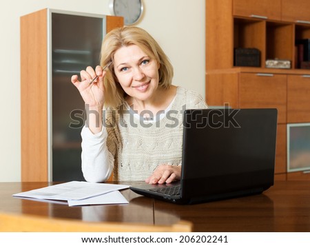 Smiling mature woman fills in the questionnaire in laptop  at home interior