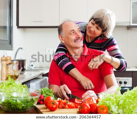 happy elderly couple cooking with vegetables in home kitchen