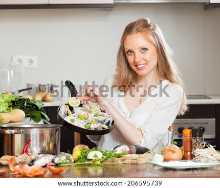 Smiling girl cooking fish with lemon in frying pan at home