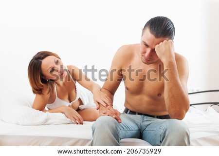 Man has sad, woman consoling him in bedroom