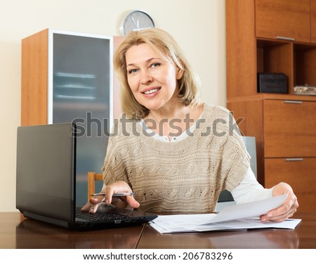 mature woman fills in the questionnaire in laptop  at home interior