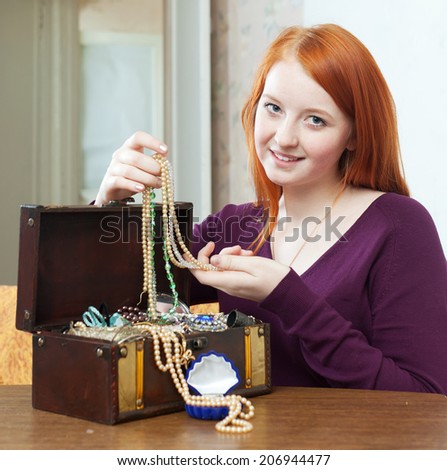 portrait of  red-headed teenager girl looks jewelry in treasure chest at home