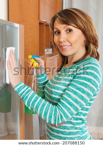 Smiling woman in green cleaning glass door of furniture