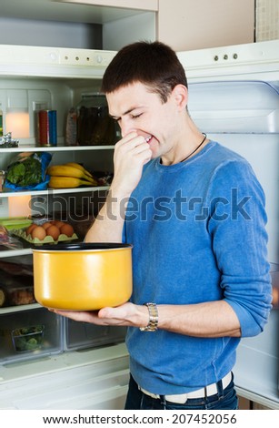 man   holding her nose because of bad smell from food near refrigerator  at kitchen