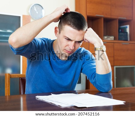 Sad frustrated man looking at financial document and scratching head