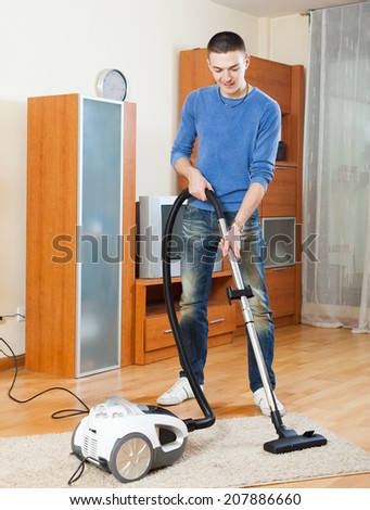 Smiling man with vacuum cleaner on parquet floor in living room