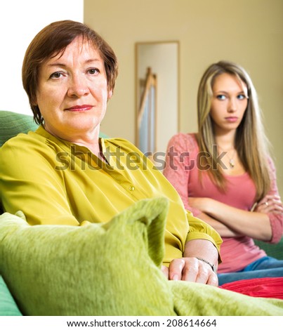 Sad elderly woman sitting on the couch next to her daughter after quarrel