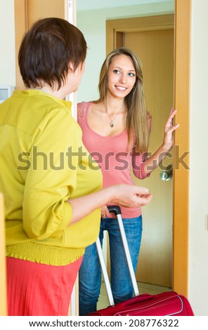 Adult daughter staying with luggage at doors and saying goodbye to mom