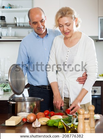 Loving elderly man and mature wife cooking vegetables together in domestic kitchen