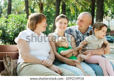 portrait of happy multigeneration family sitting on bench in sunny summer day