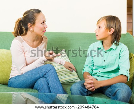 Serious mother scolding teenage son in living room