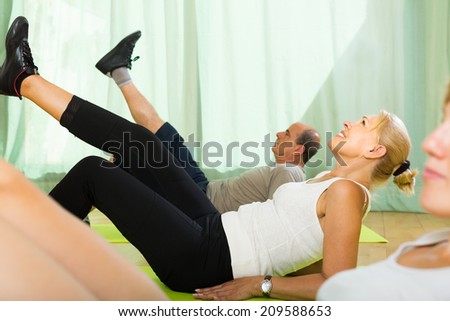 Positive smiling elderly couple practicing body bending at gym