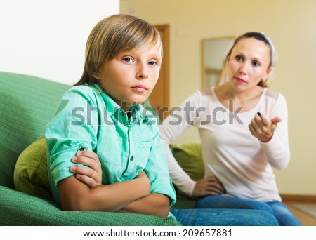 Angry mother scolding teenager son in living room at home. Focus on boy