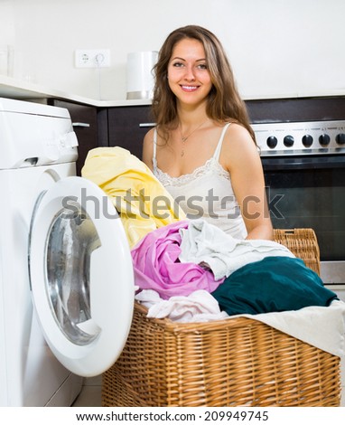 Home laundry. Beautiful long-haired girl using washing machine at home kitchen