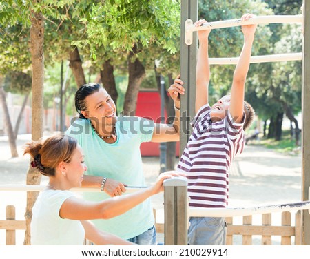 Happy couple with teenage son  training on pull-up bar   in the yard