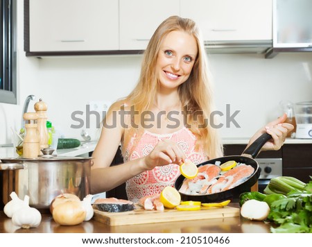 Smiling girl cooking salmon fish with lemon in frying pan at  kitchen