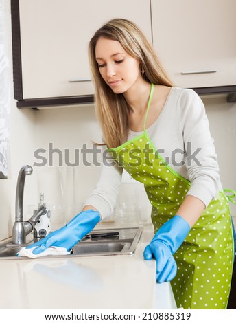 woman in apron cleaning  furniture with rag in kitchen at home