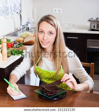 Woman weighing chocolate on kitchen scales at table
