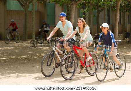 Happy parents with teenager son going by bicycles through city in summer day