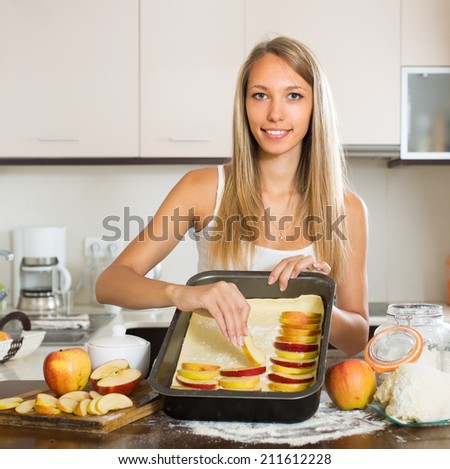 Young smiling woman preparing apple cake in domestic kitchen