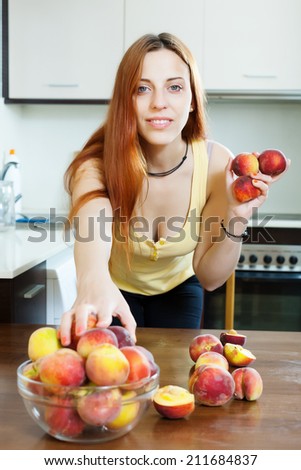 pretty long-haired woman taking peaches at table in home interior