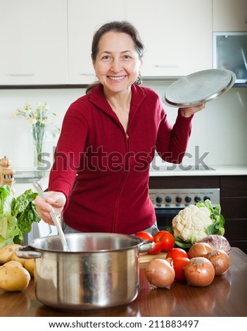 Happy mature woman cooking lent diet soup in her kitchen