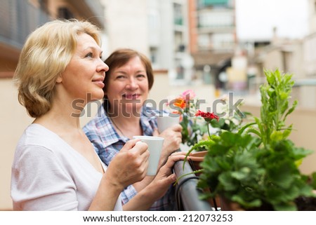 Smiling senior female pensioners relaxing with cup of coffee on balcony
