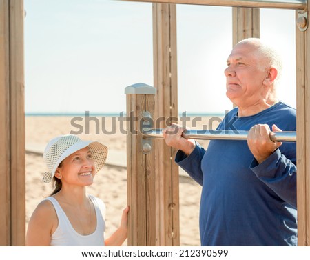Happy senior man and mature woman training with pull-up bar at playground