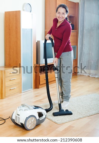 Happy mature woman cleaning with vacuum cleaner   in living room