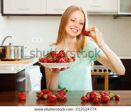 Happy blonde long-haired woman eating strawberry