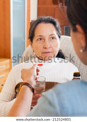 Woman giving the cough syrup to elderly mother