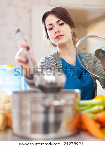 young woman tests food with ladle in the kitchen at home