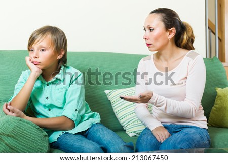 Angry mother scolding naughty teenage son in living room at home. Focus on woman