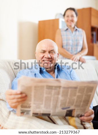 Happy mature couple reading newspaper  together at home interior