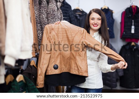 Cute young woman choosing jacket at clothing store